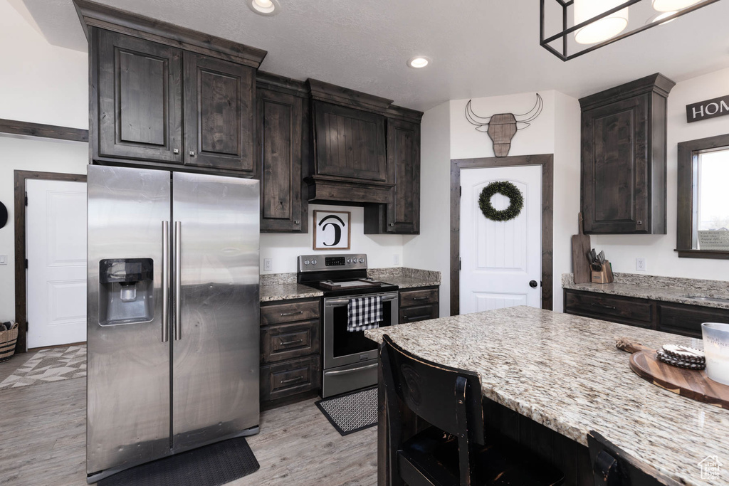 Kitchen featuring light stone counters, light wood-style flooring, dark brown cabinets, and stainless steel appliances