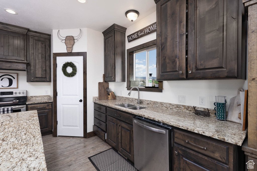 Kitchen featuring dark brown cabinetry, a sink, stainless steel appliances, recessed lighting, and wood finished floors