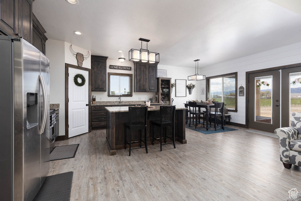 Kitchen with a kitchen island, dark brown cabinets, a breakfast bar area, light wood finished floors, and appliances with stainless steel finishes