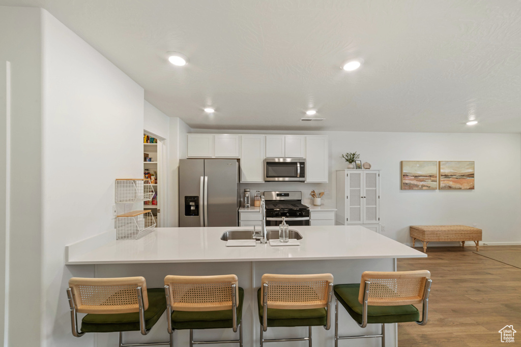 Kitchen featuring white cabinets, a kitchen breakfast bar, stainless steel appliances, a peninsula, and wood finished floors