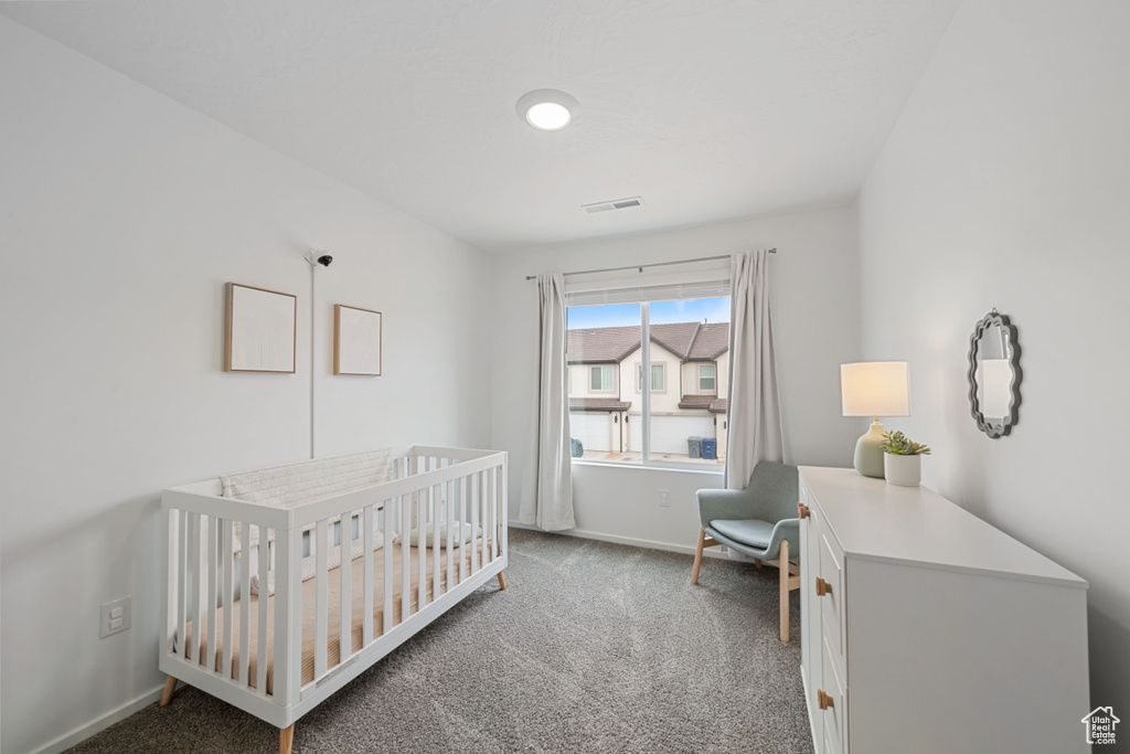 Carpeted bedroom featuring baseboards, visible vents, and a crib