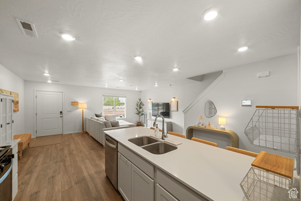 Kitchen featuring a sink, open floor plan, dark wood-type flooring, stainless steel dishwasher, and visible vents