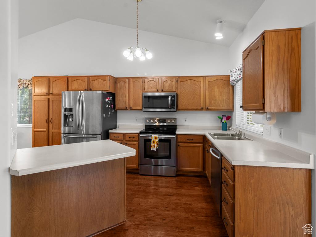 Kitchen with brown cabinetry, appliances with stainless steel finishes, dark wood finished floors, a sink, and high vaulted ceiling