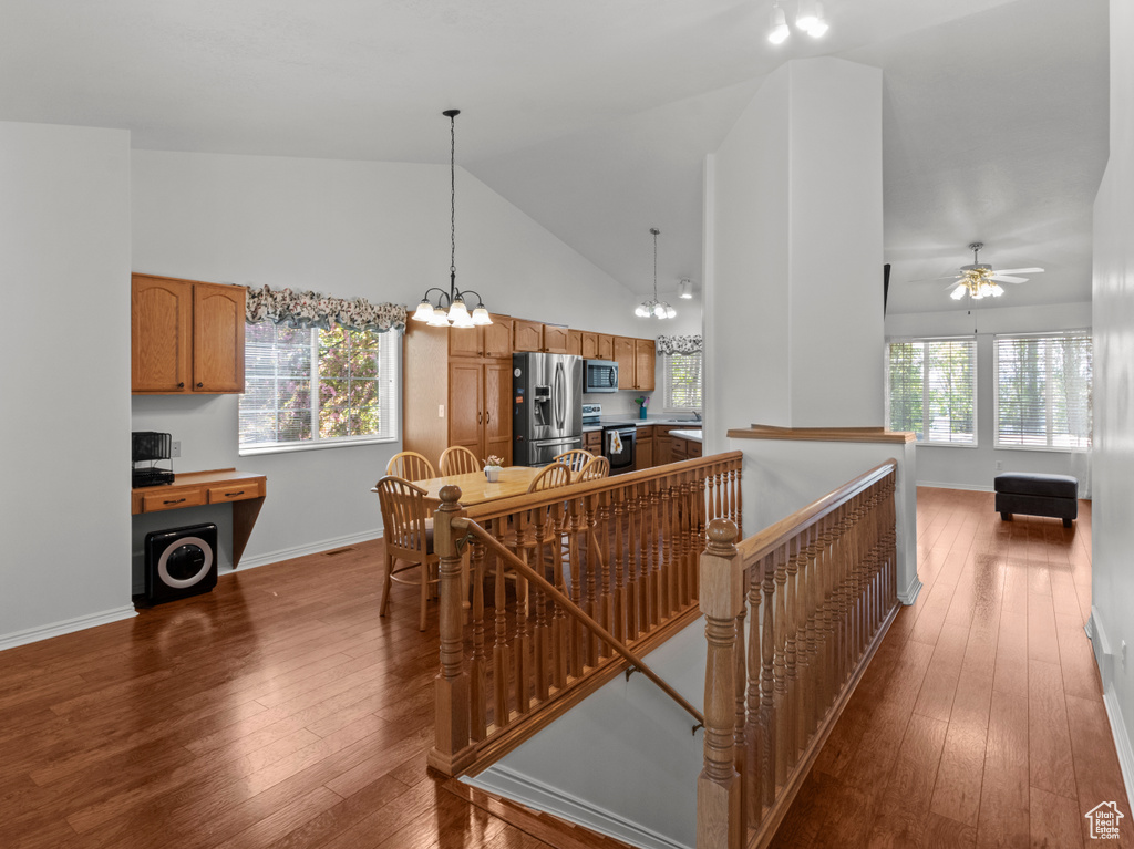 Interior space with dark wood-style flooring, appliances with stainless steel finishes, hanging light fixtures, high vaulted ceiling, and brown cabinetry