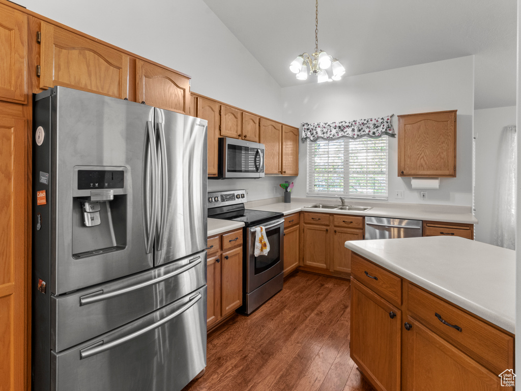 Kitchen featuring appliances with stainless steel finishes, dark wood finished floors, a sink, light countertops, and an inviting chandelier