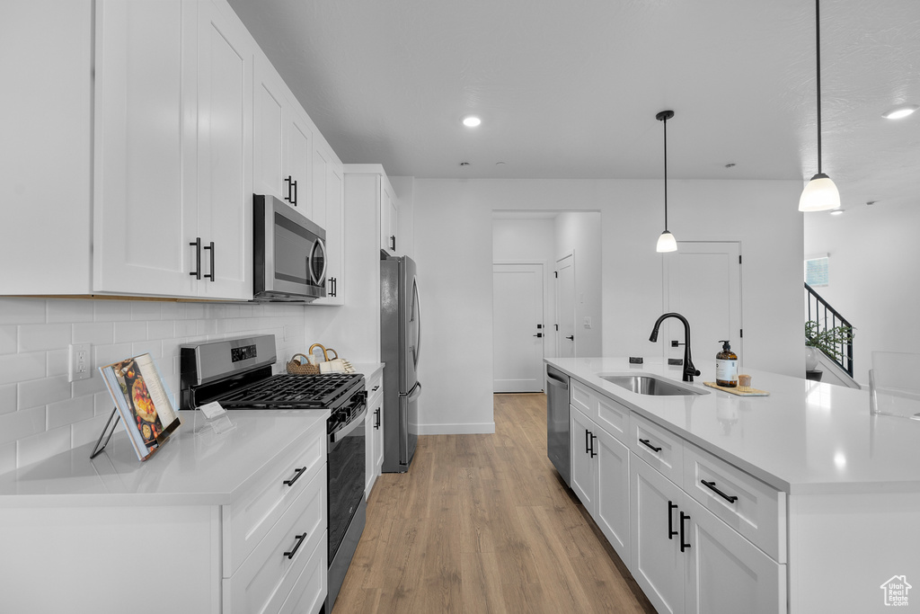Kitchen with white cabinets, appliances with stainless steel finishes, a sink, light wood-style flooring, and decorative backsplash