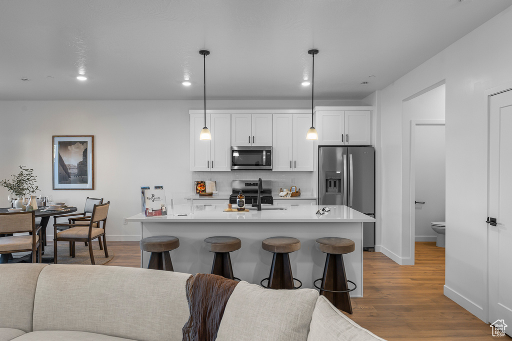 Kitchen with backsplash, appliances with stainless steel finishes, a sink, baseboards, and light wood-style floors