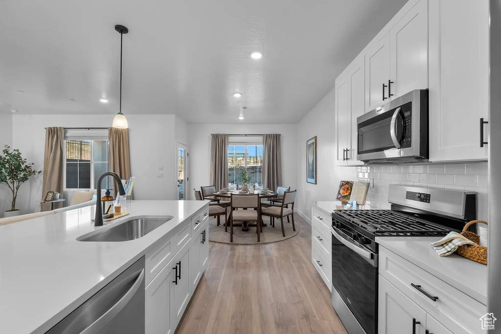 Kitchen featuring light wood-style floors, light countertops, white cabinets, a sink, and appliances with stainless steel finishes