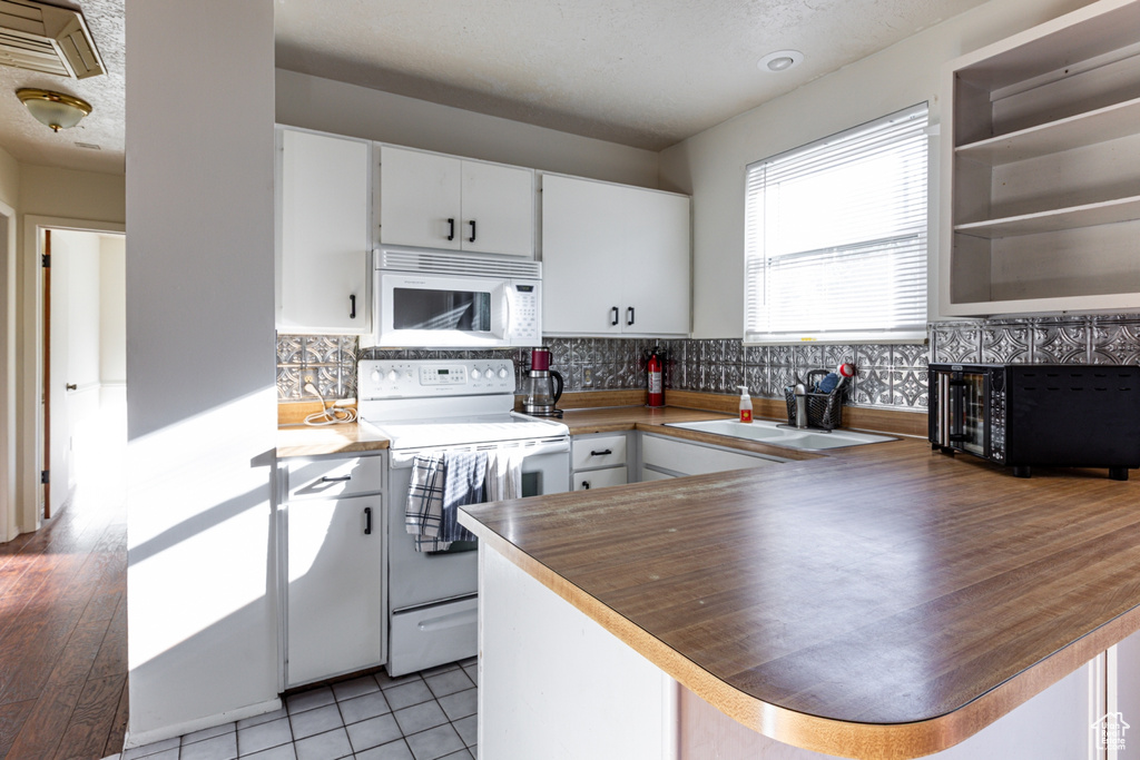 Kitchen featuring decorative backsplash, white cabinetry, a peninsula, and white appliances