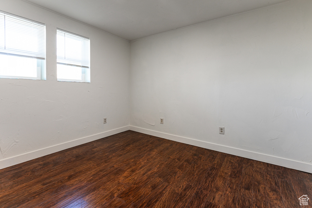 Spare room featuring baseboards and dark wood-type flooring