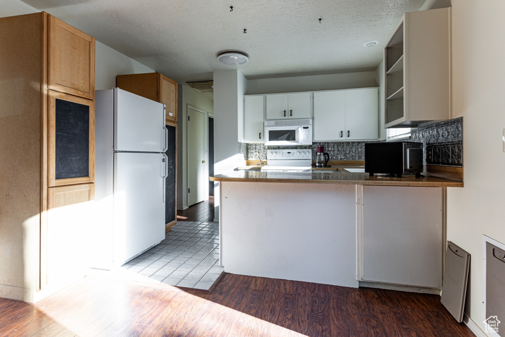 Kitchen featuring open shelves, white appliances, a peninsula, decorative backsplash, and wood finished floors