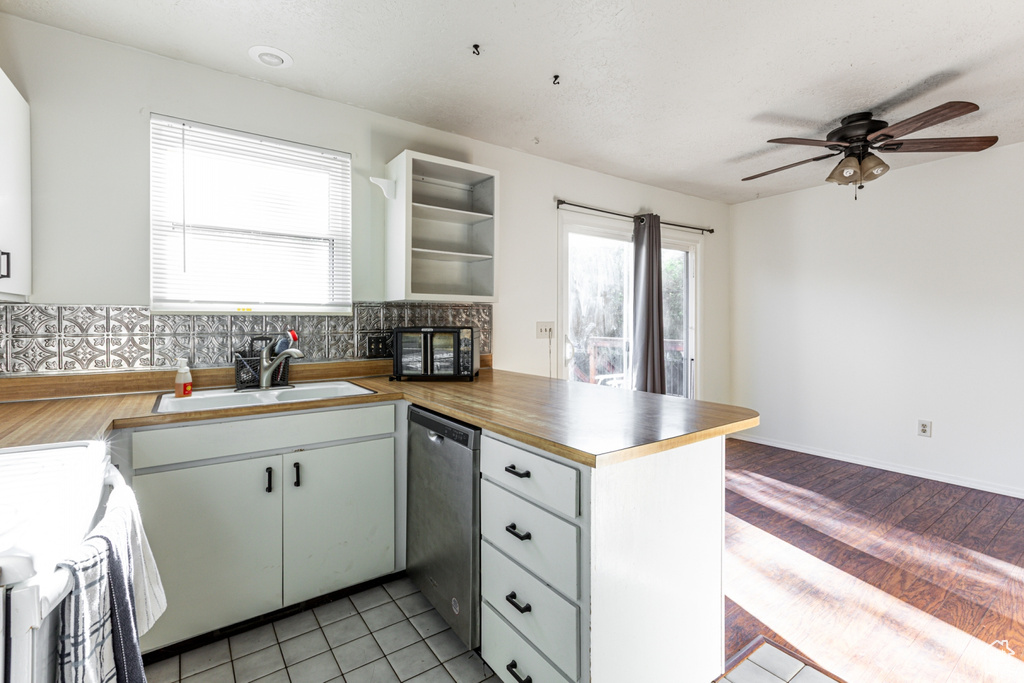 Kitchen featuring decorative backsplash, ceiling fan, stainless steel dishwasher, a sink, and a peninsula