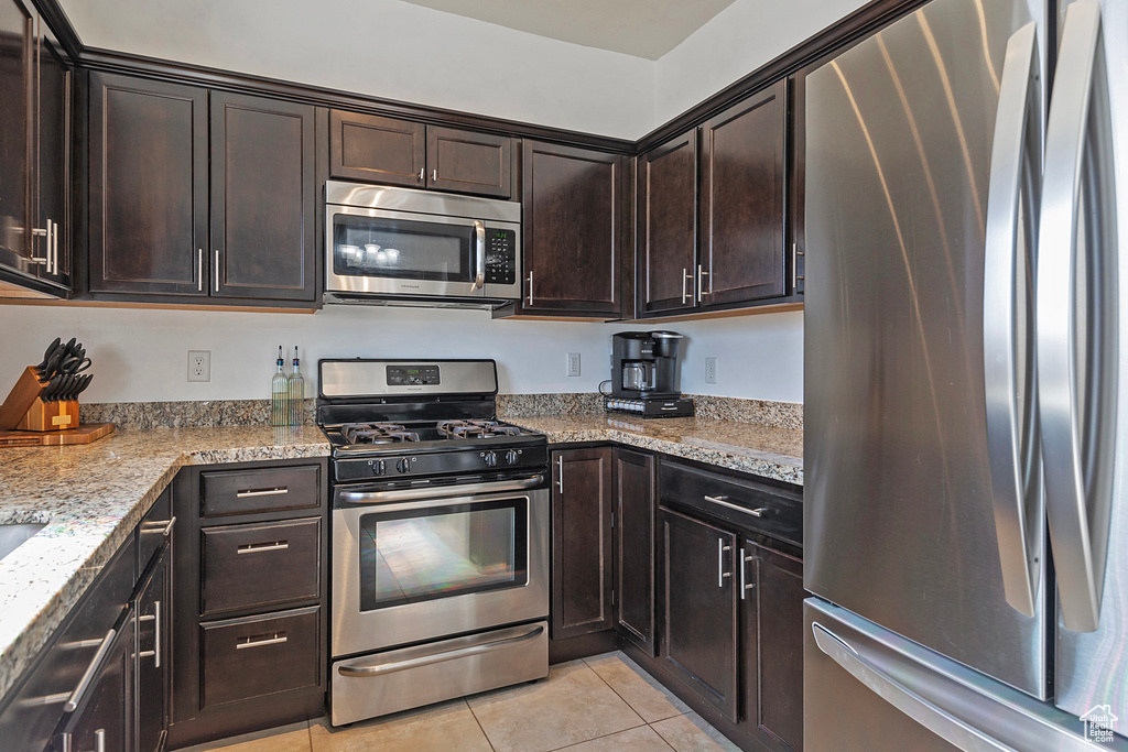 Kitchen with stainless steel appliances, dark brown cabinetry, light stone counters, and light tile patterned floors