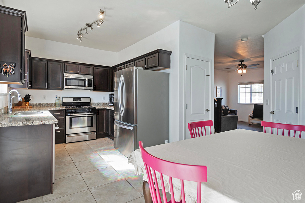 Kitchen with light stone countertops, dark brown cabinets, a sink, light tile patterned floors, and stainless steel appliances