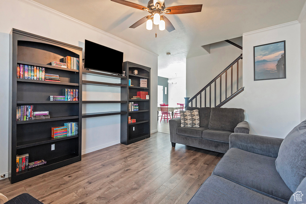 Living area featuring crown molding, stairs, ceiling fan with notable chandelier, and wood finished floors