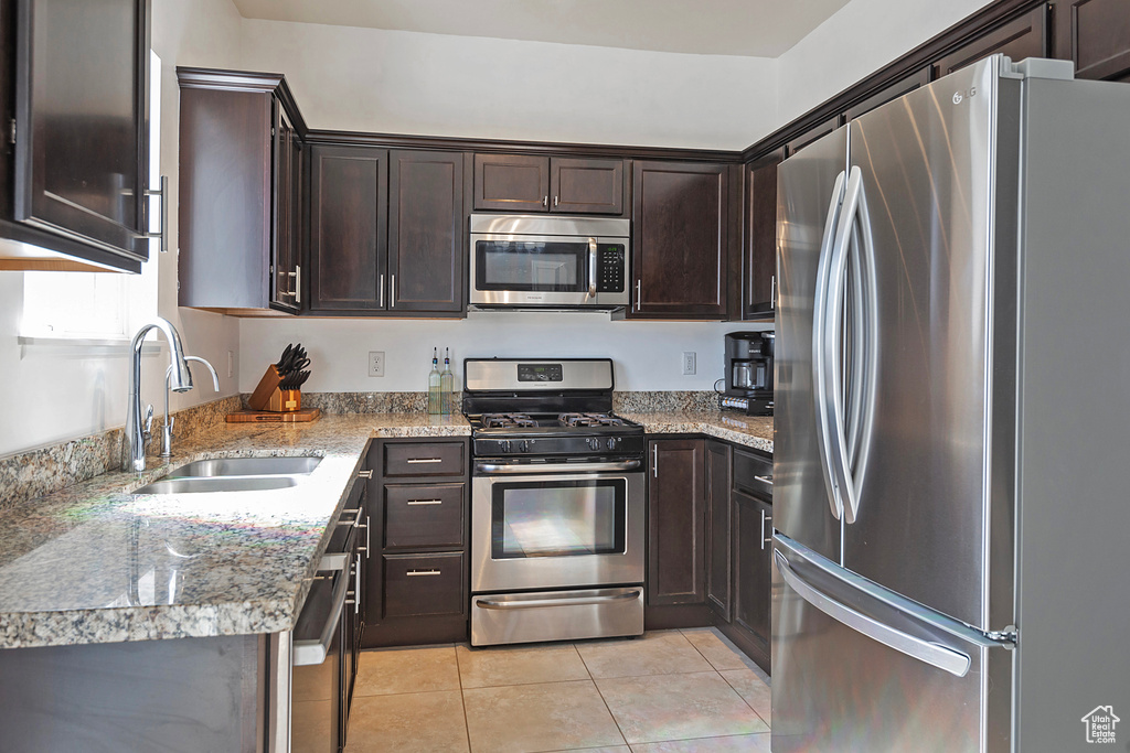 Kitchen with light tile patterned flooring, dark brown cabinets, light stone counters, a sink, and appliances with stainless steel finishes