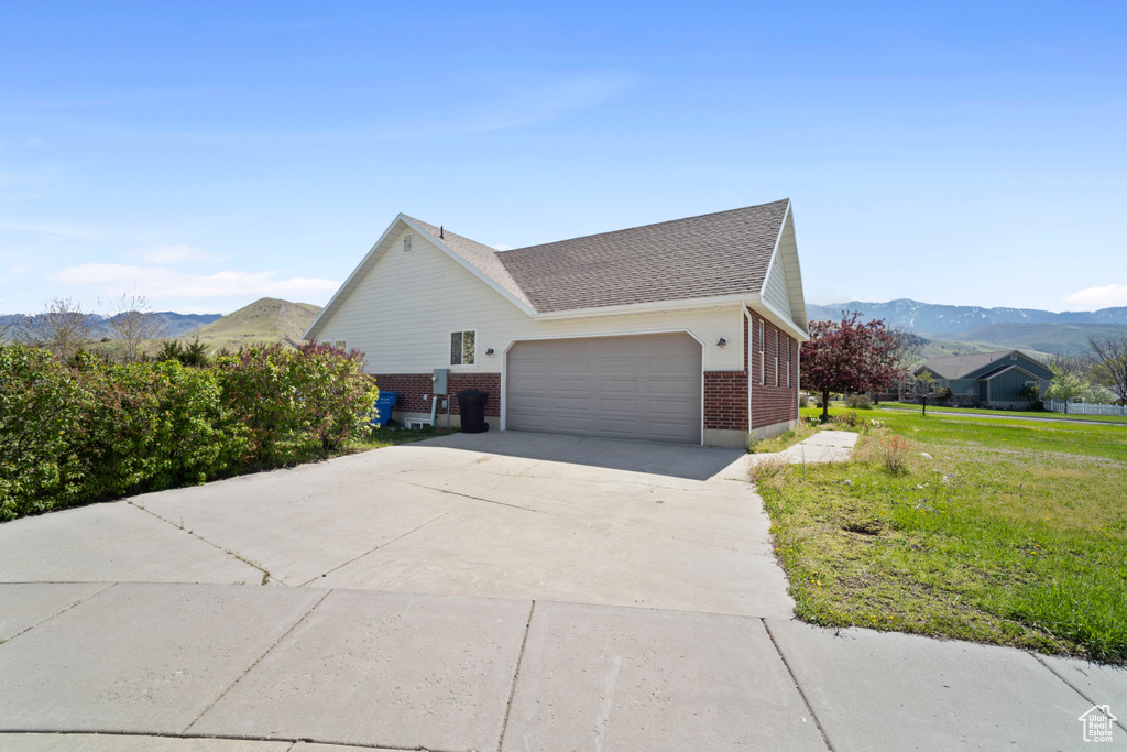 View of home's exterior with brick siding, a garage, a mountain view, a lawn, and driveway