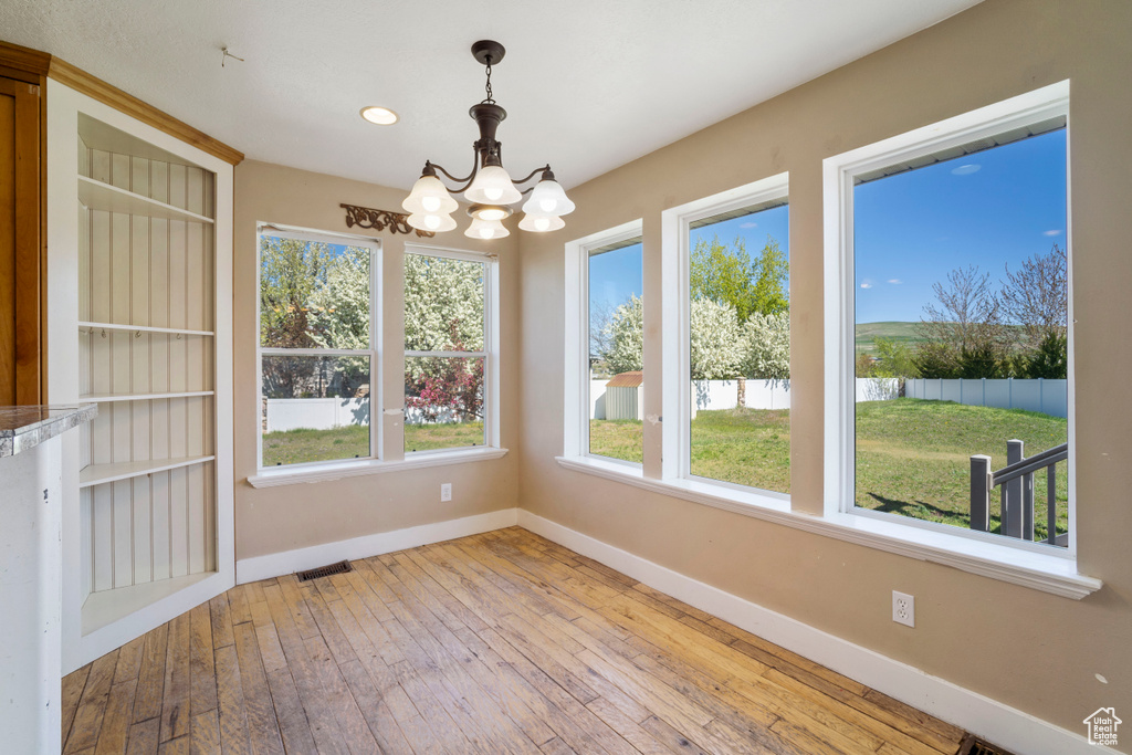 Unfurnished dining area with baseboards, a notable chandelier, hardwood / wood-style flooring, and visible vents
