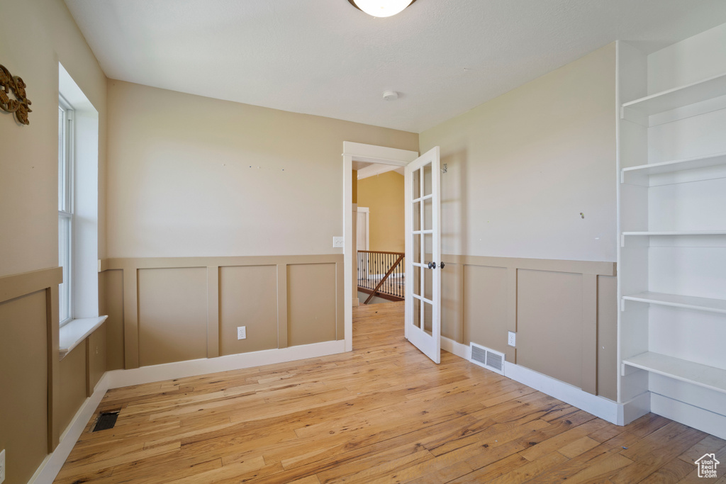 Empty room featuring wood-type flooring, visible vents, french doors, and a decorative wall