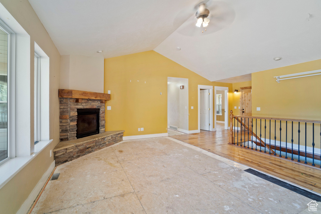 Unfurnished living room with a ceiling fan, baseboards, a stone fireplace, and lofted ceiling
