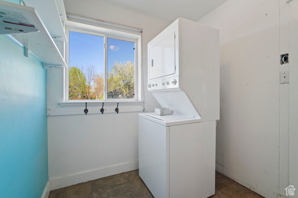 Laundry room featuring laundry area, stone finish flooring, baseboards, and stacked washer / drying machine