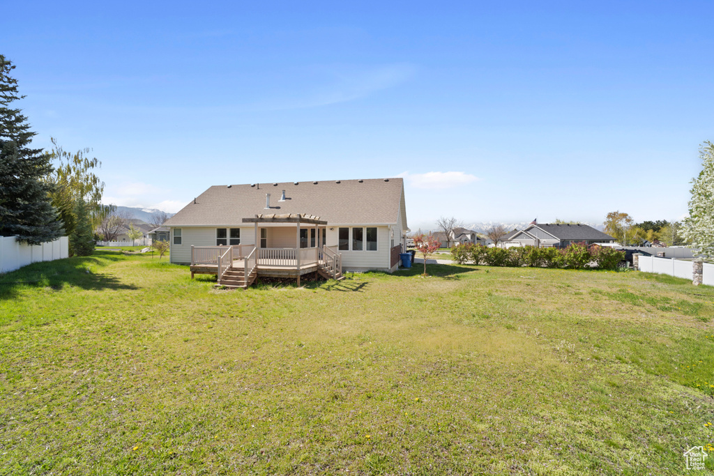 Back of house with fence, a pergola, a deck, roof with shingles, and a lawn
