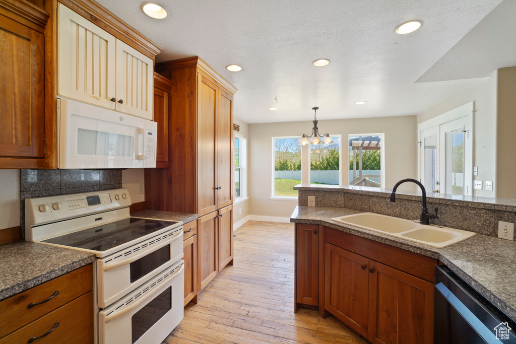 Kitchen with white appliances, dark countertops, a notable chandelier, and a sink