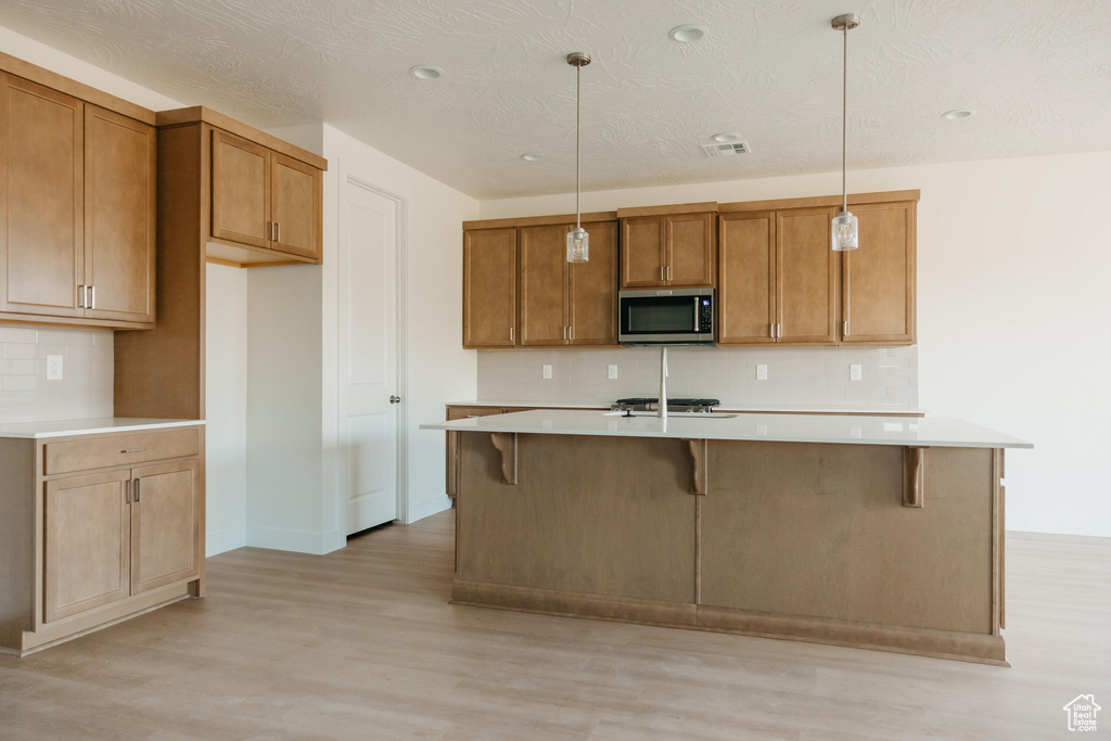 Kitchen with light countertops, backsplash, stainless steel appliances, and light wood-type flooring