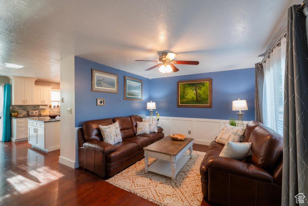 Living area with ceiling fan, wainscoting, dark wood-style flooring, and a textured ceiling