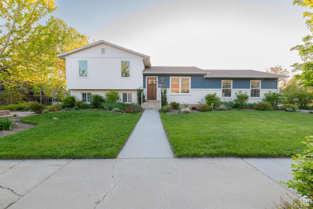 Split level home featuring fence, a front lawn, and brick siding