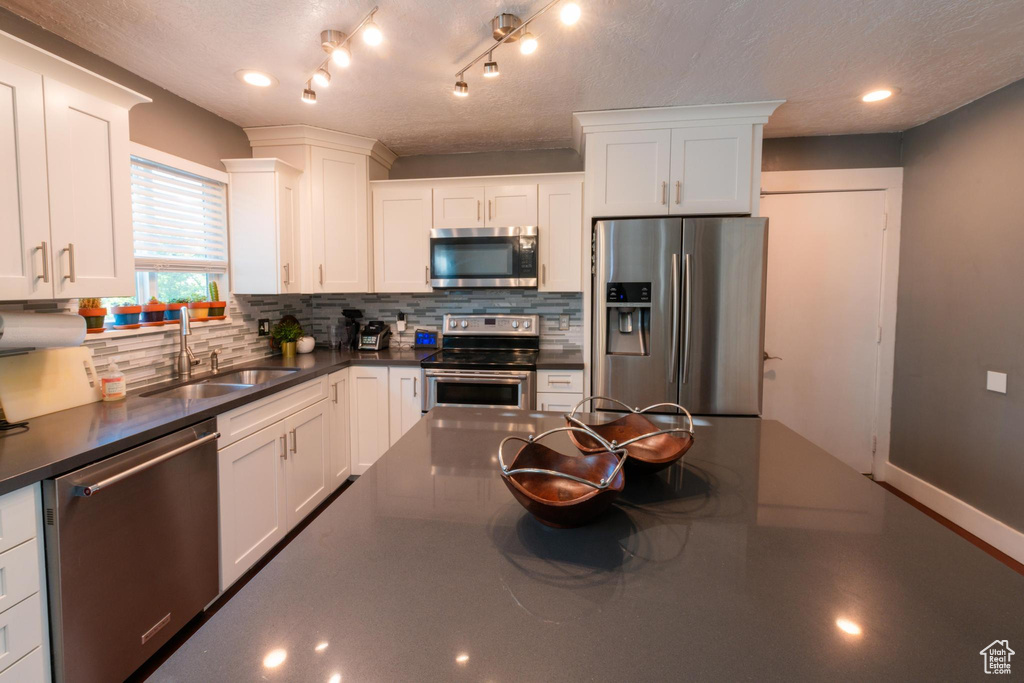 Kitchen with decorative backsplash, dark countertops, white cabinetry, a sink, and appliances with stainless steel finishes
