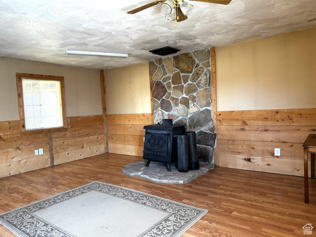 Unfurnished living room with wooden walls, wainscoting, and a wood stove