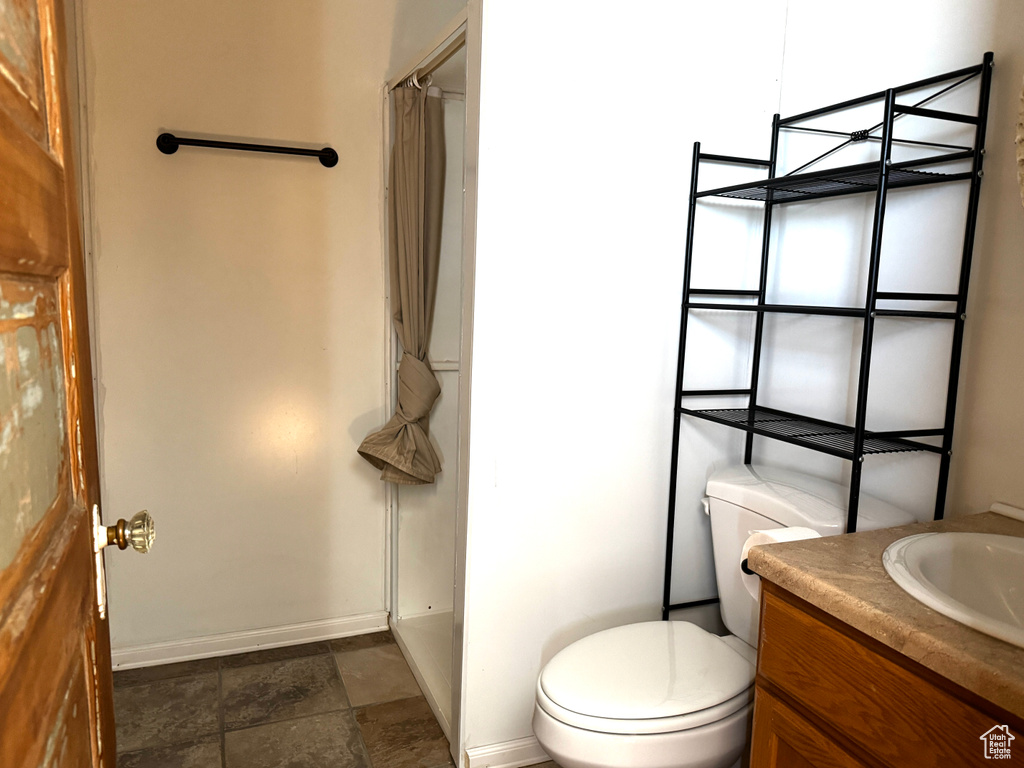 Bathroom with baseboards, stone finish flooring, toilet, and a shower with shower curtain