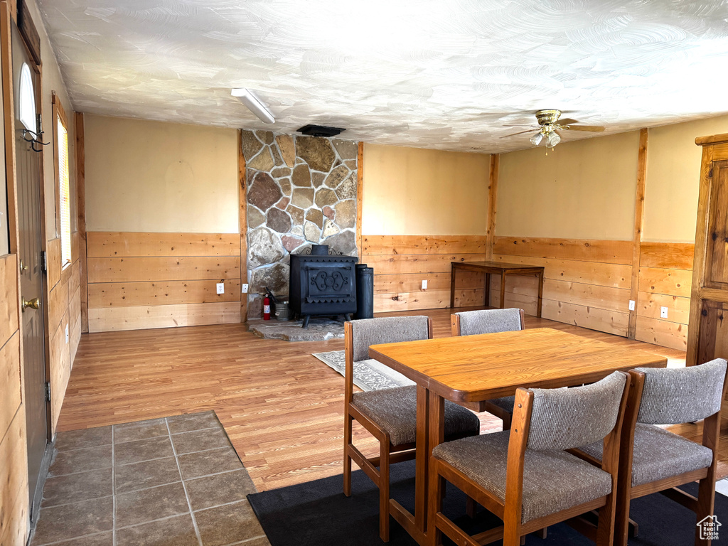 Dining room featuring wood walls, wainscoting, a wood stove, wood finished floors, and a ceiling fan