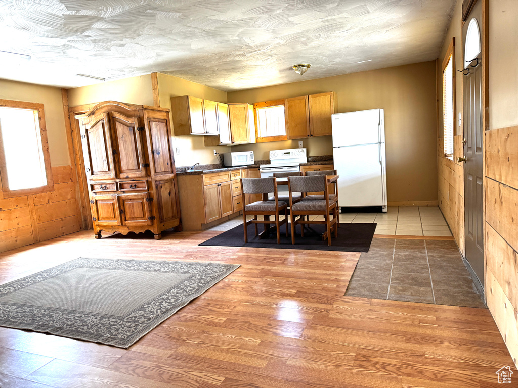 Kitchen with light wood-type flooring, dark countertops, a wainscoted wall, and white appliances