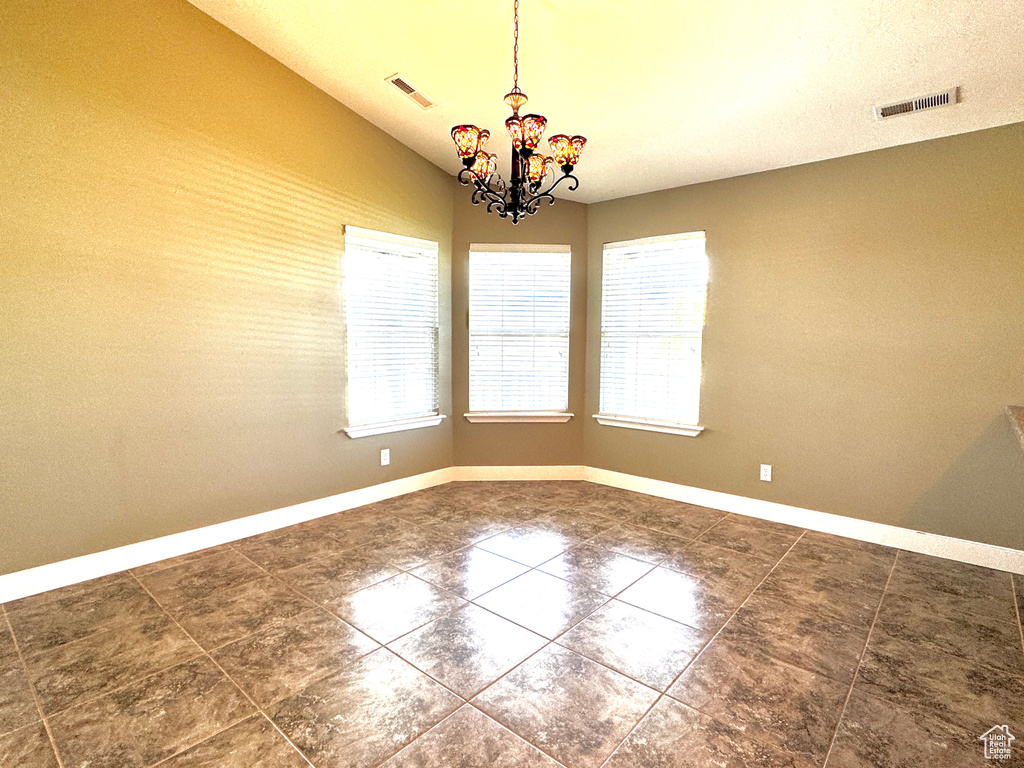 Spare room featuring an inviting chandelier, baseboards, dark tile patterned flooring, and visible vents