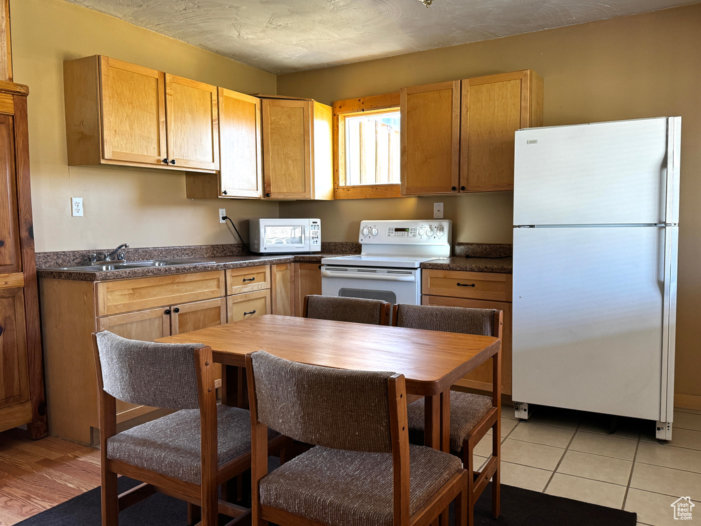 Kitchen featuring a sink, dark countertops, light tile patterned floors, and white appliances