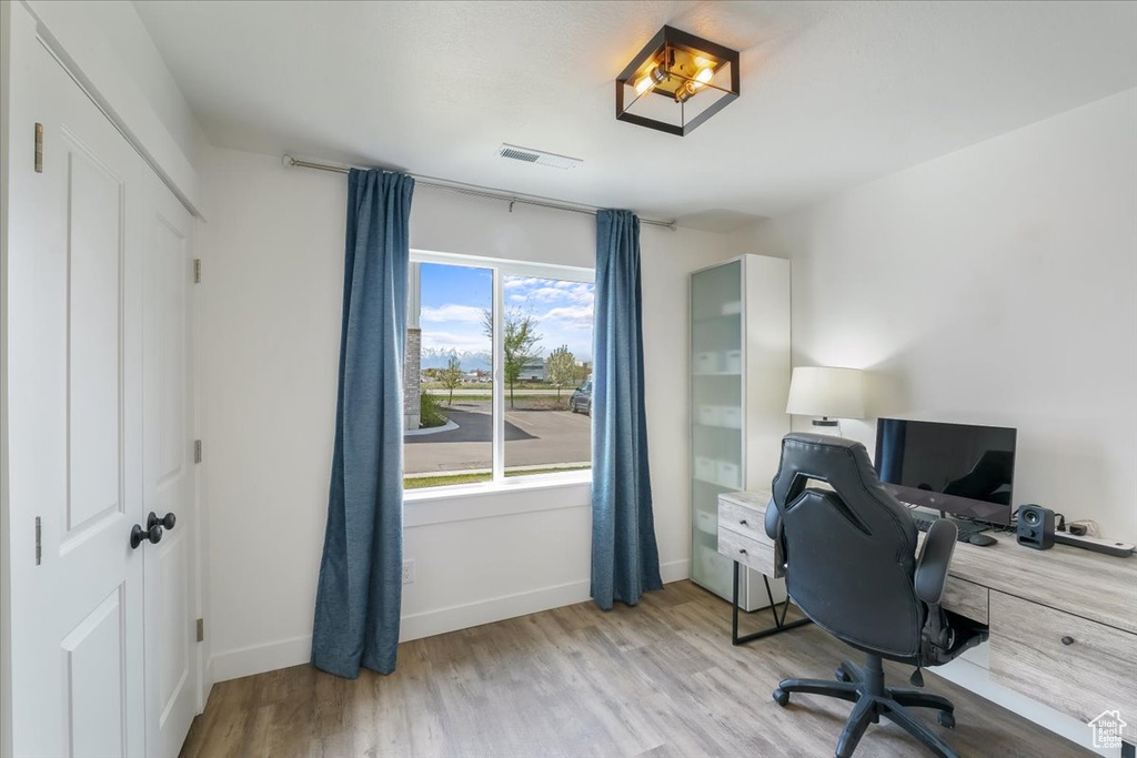 Office area with light wood-style floors, baseboards, and visible vents