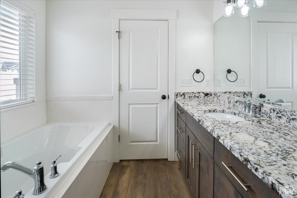 Full bath with vanity, a garden tub, and wood finished floors