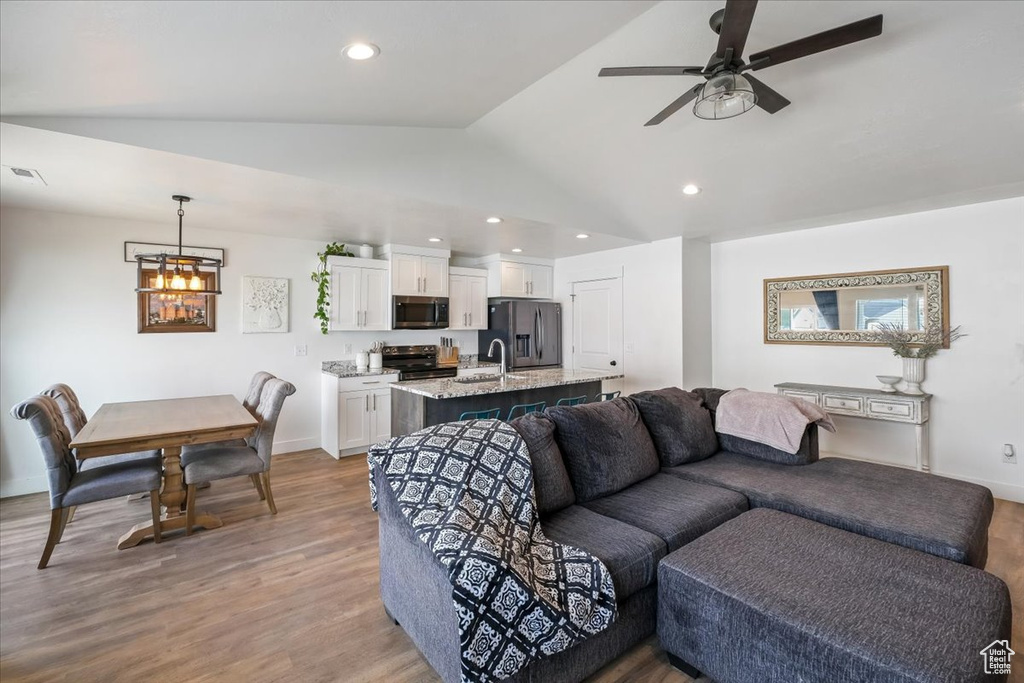 Living room featuring recessed lighting, vaulted ceiling, wood finished floors, and ceiling fan with notable chandelier