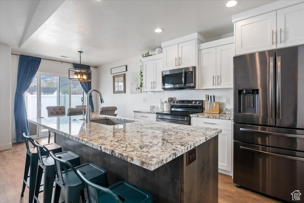 Kitchen featuring white cabinets, appliances with stainless steel finishes, a sink, an island with sink, and wood finished floors