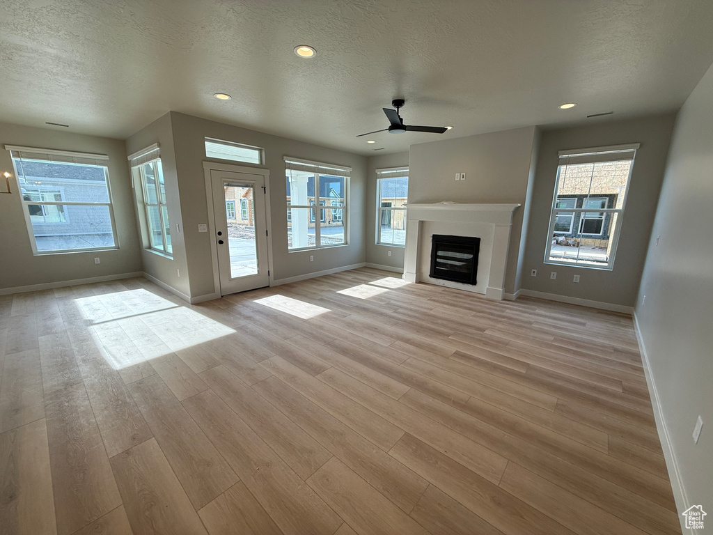 Unfurnished living room with ceiling fan, baseboards, light wood finished floors, a textured ceiling, and recessed lighting