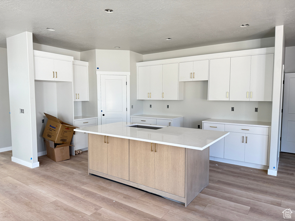 Kitchen with baseboards, white cabinets, a kitchen island, and light wood-style flooring
