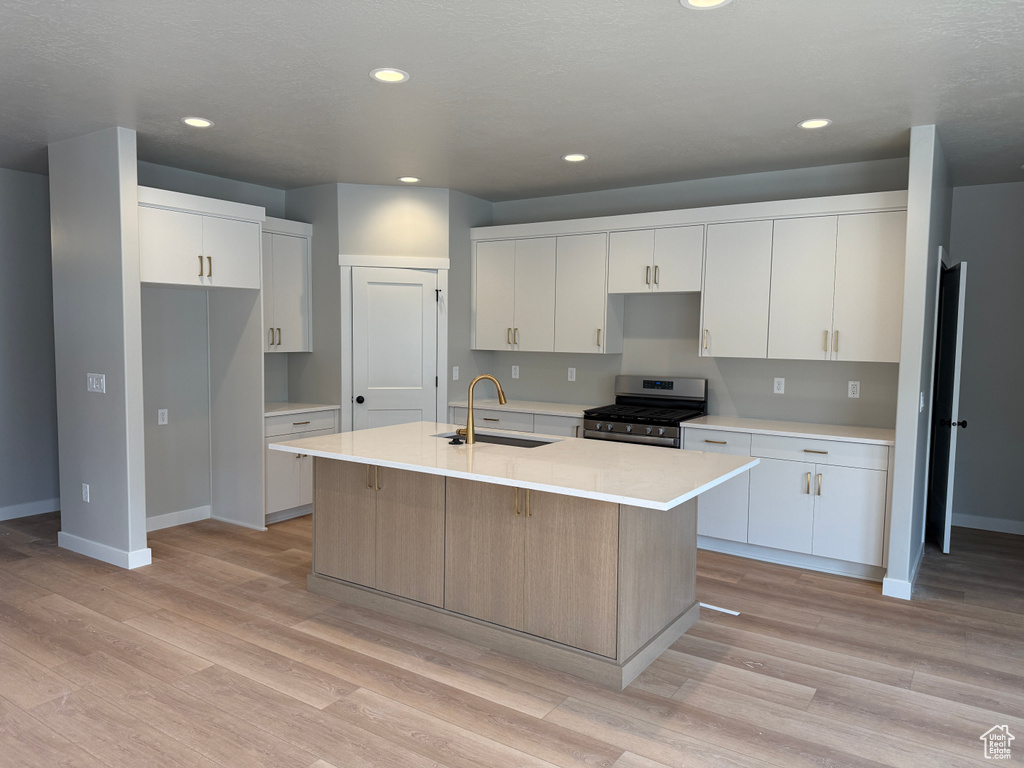 Kitchen featuring a sink, stainless steel range with gas cooktop, an island with sink, light wood-style floors, and recessed lighting