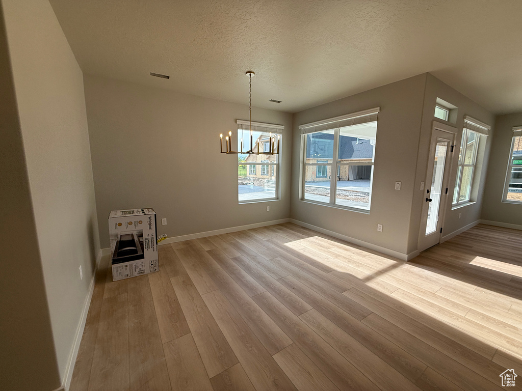 Unfurnished dining area featuring a chandelier, heating unit, wood finished floors, baseboards, and a textured ceiling