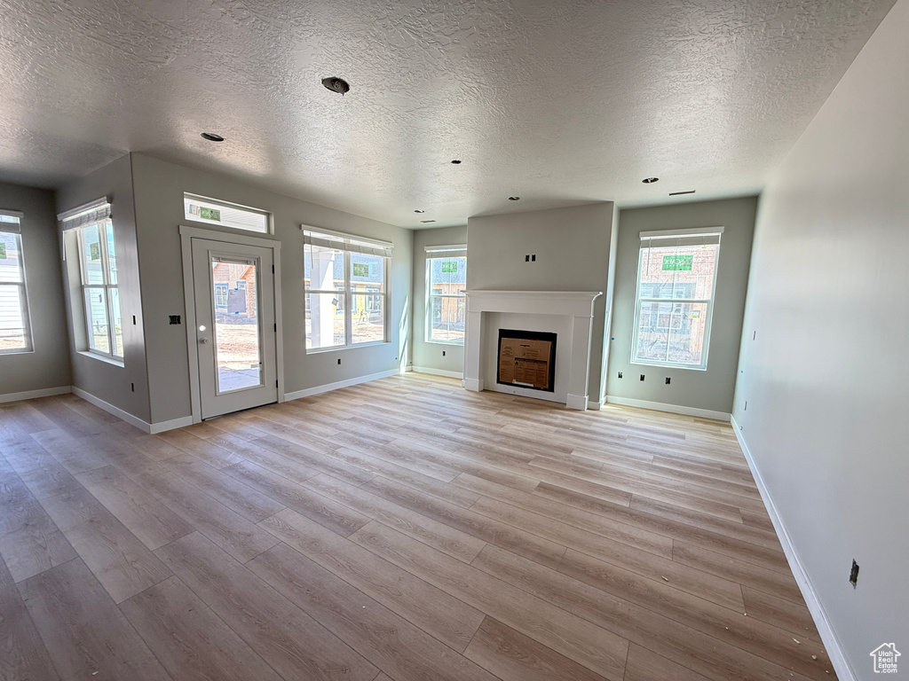 Unfurnished living room featuring a textured ceiling, baseboards, light wood-style flooring, and a fireplace
