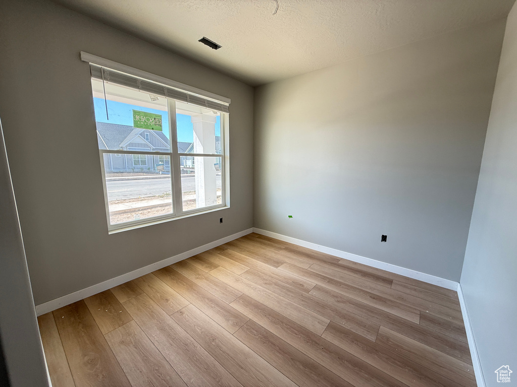 Spare room featuring a textured ceiling, baseboards, and light wood-style floors