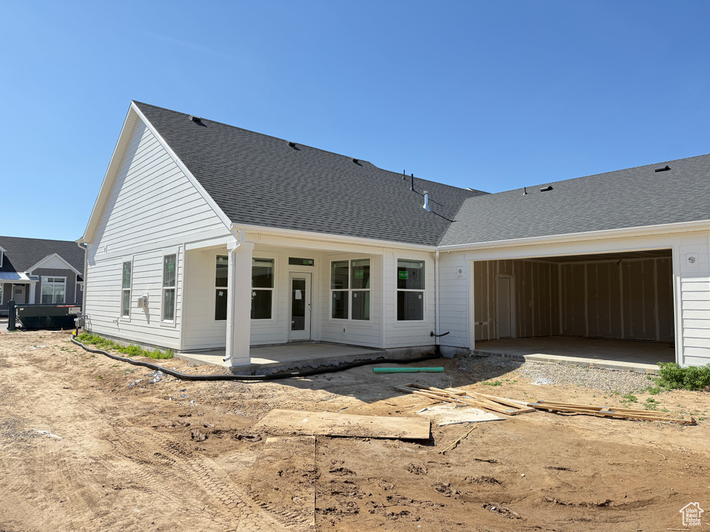 Back of property featuring a garage, a shingled roof, and a patio area