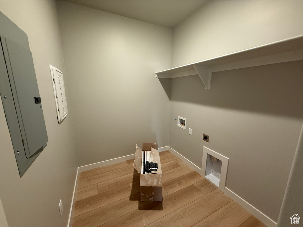 Laundry area with hookup for an electric dryer, hookup for a washing machine, light wood-style flooring, electric panel, and baseboards