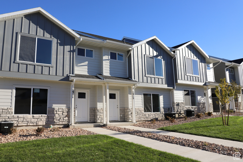 View of property featuring board and batten siding, central AC, stone siding, and a front lawn